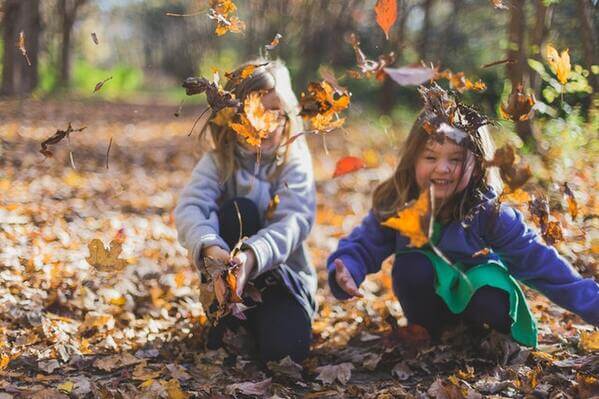 des enfants rigolent avec des feuilles mortes